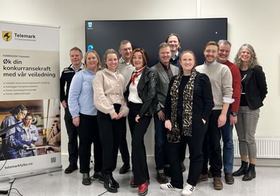 Personer står samlet ved side av en roll-up. Roll-up viser illustrasjons bilde og tekst om hva Forregion Telemarks kompetansemeglere kan bidra med