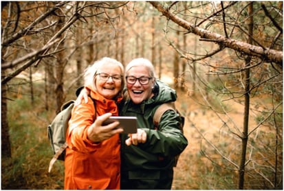 To smilende kvinner i skogen står sammen og ser på en mobil  