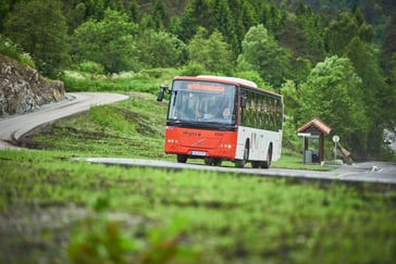 Bilde av en orange og hvit buss som kjører en svingete vei, omgitt av grønn vegetasjon