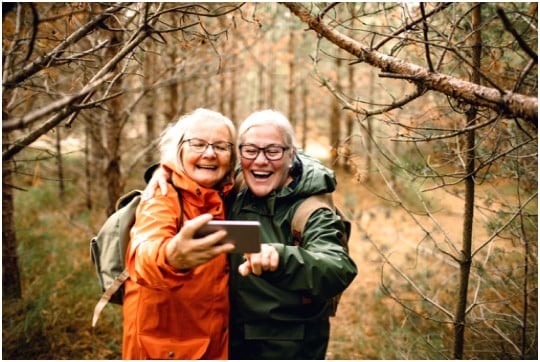 To smilende kvinner i skogen står sammen og ser på en mobil  