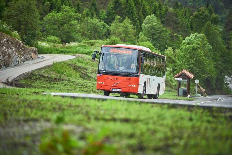 Bilde av en orange og hvit buss som kjører en svingete vei, omgitt av grønn vegetasjon
